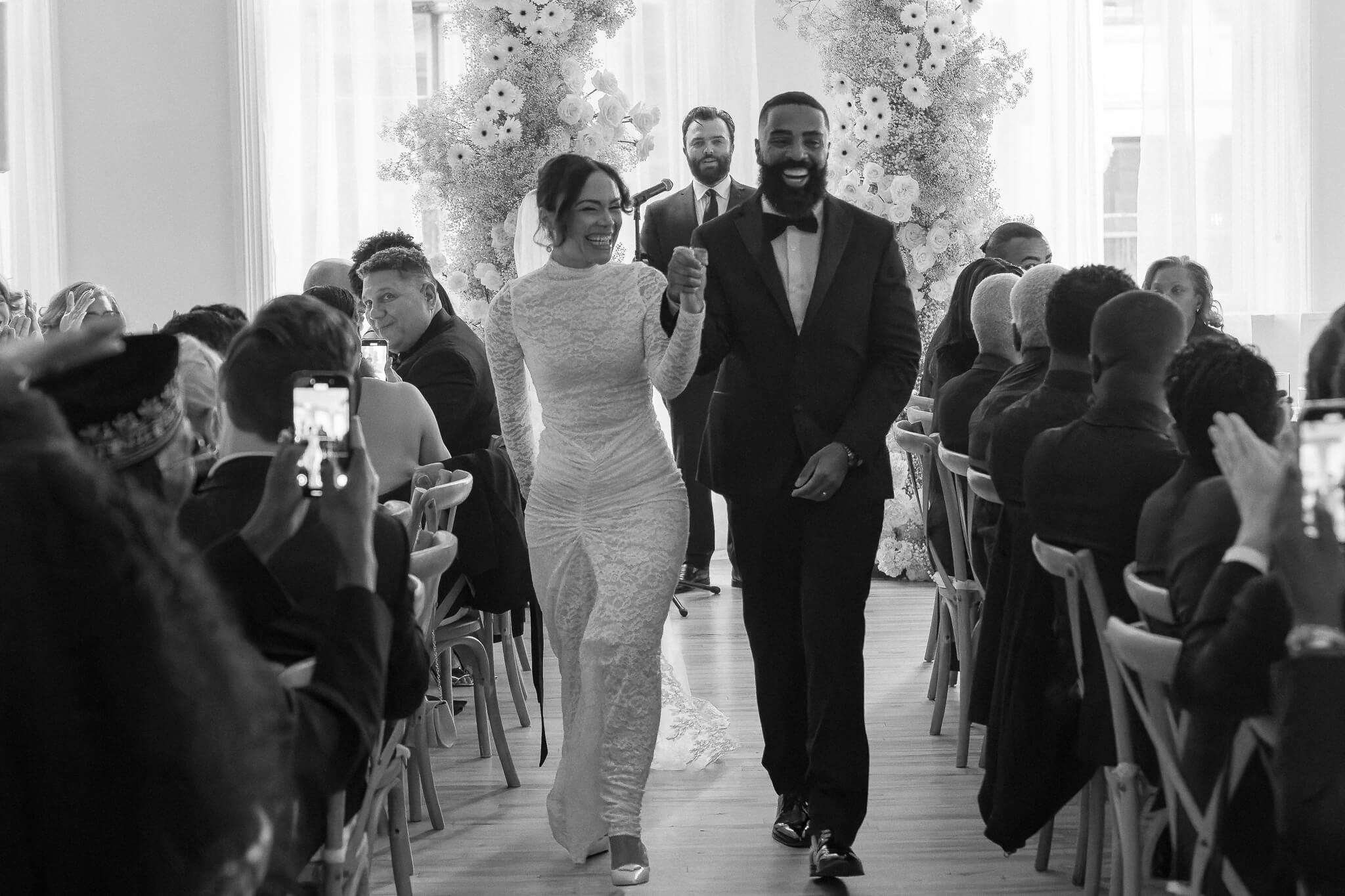 nyc wedding couple laughing and acknowledging their guests walking down aisle after ceremony located in the venue NYC Home Studios in black and white