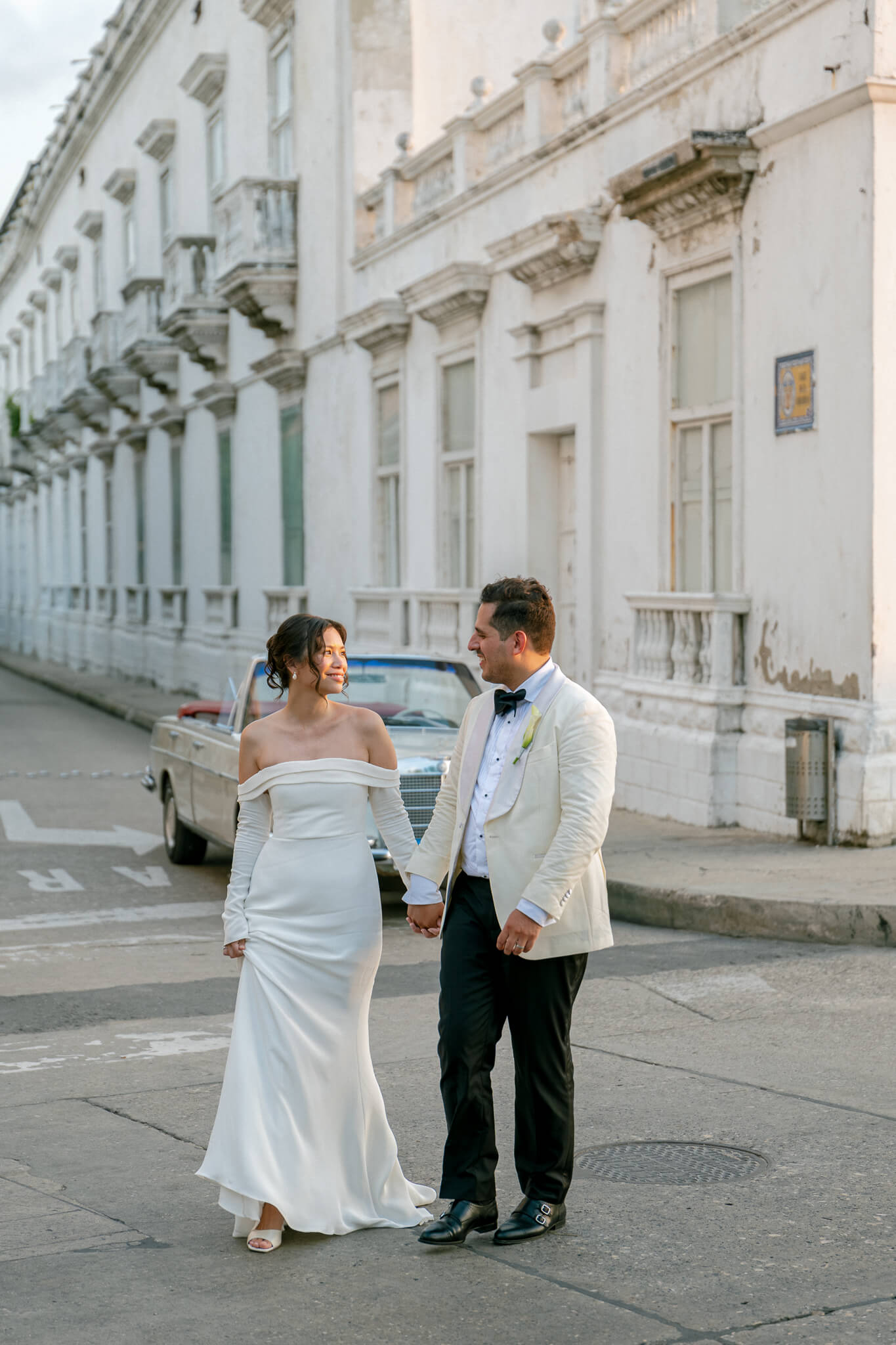 wedding couple walking hand by hand in the cartagena streets, bride has white dress and groom has white suit