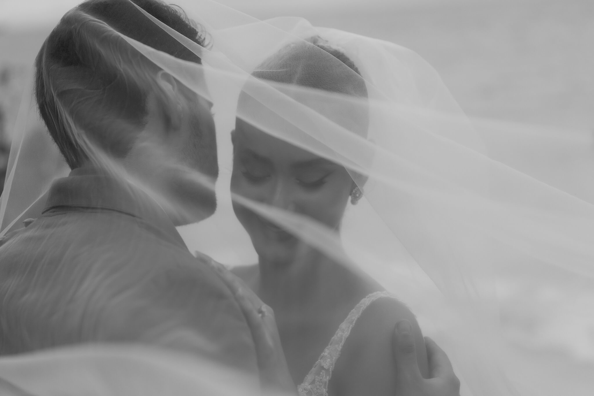 Scenic and whimsical wedding couple with the wind bring the brides vail to cover both and create an intimate moment