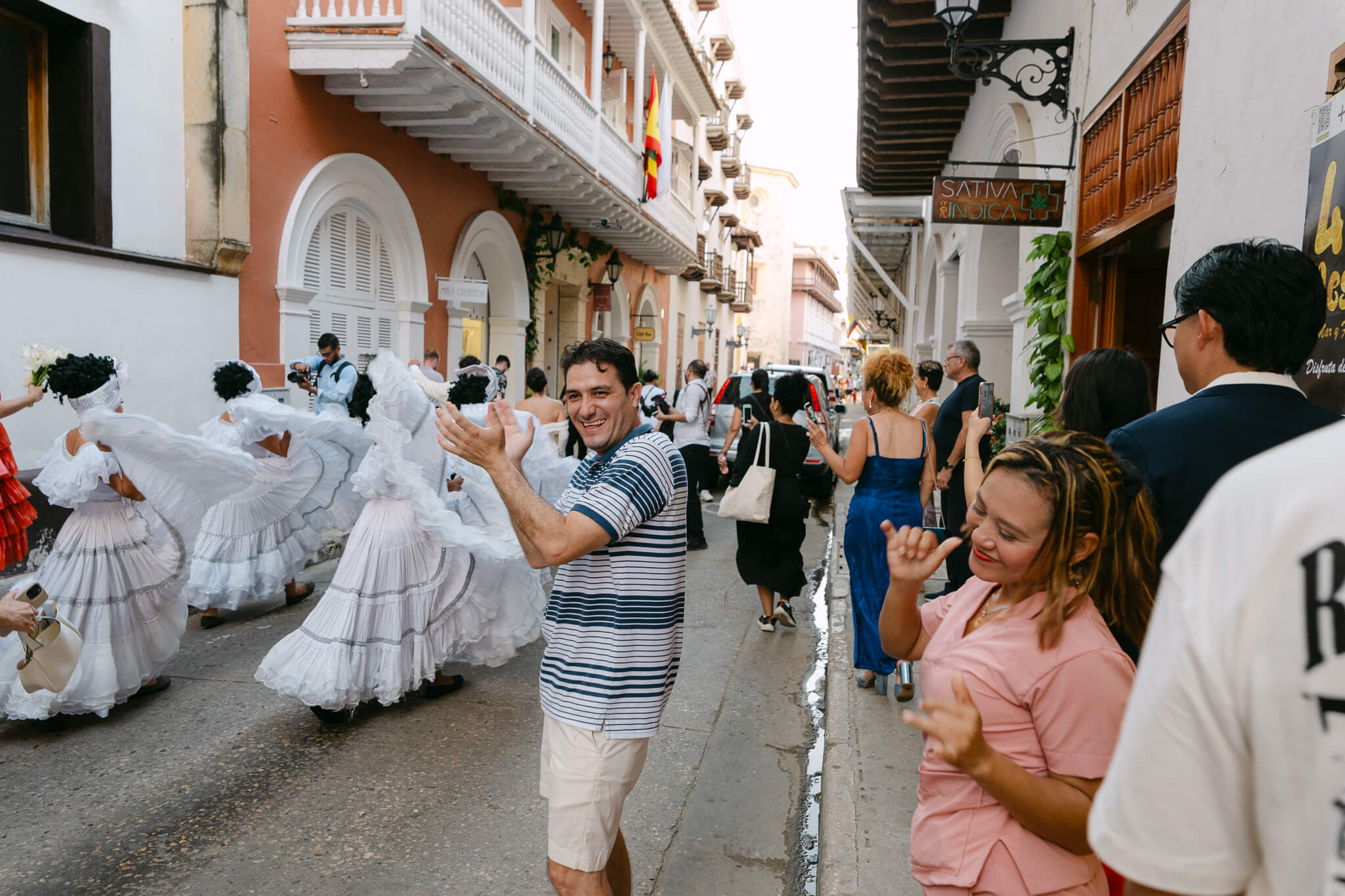 cartagena people on the street dancing as a wedding parade goes past them and a lady in pink is really vibing with the music and a man next to he rin blue is enjoying the party as well