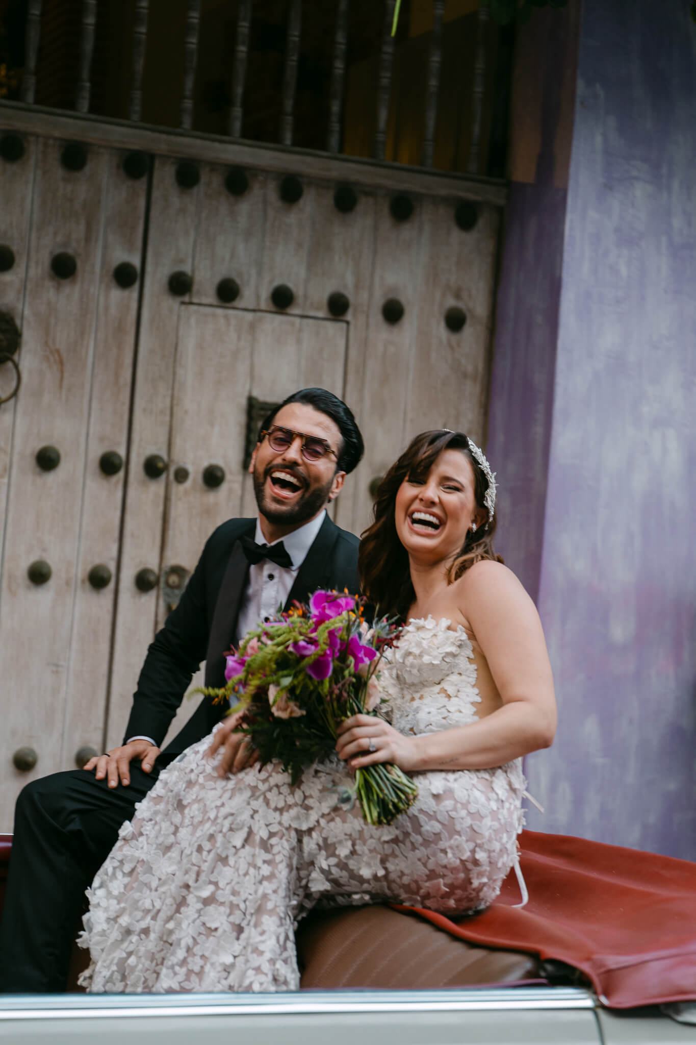 cartagena wedding couple laughing together enjoying their day in a vinatge car with a purple house background