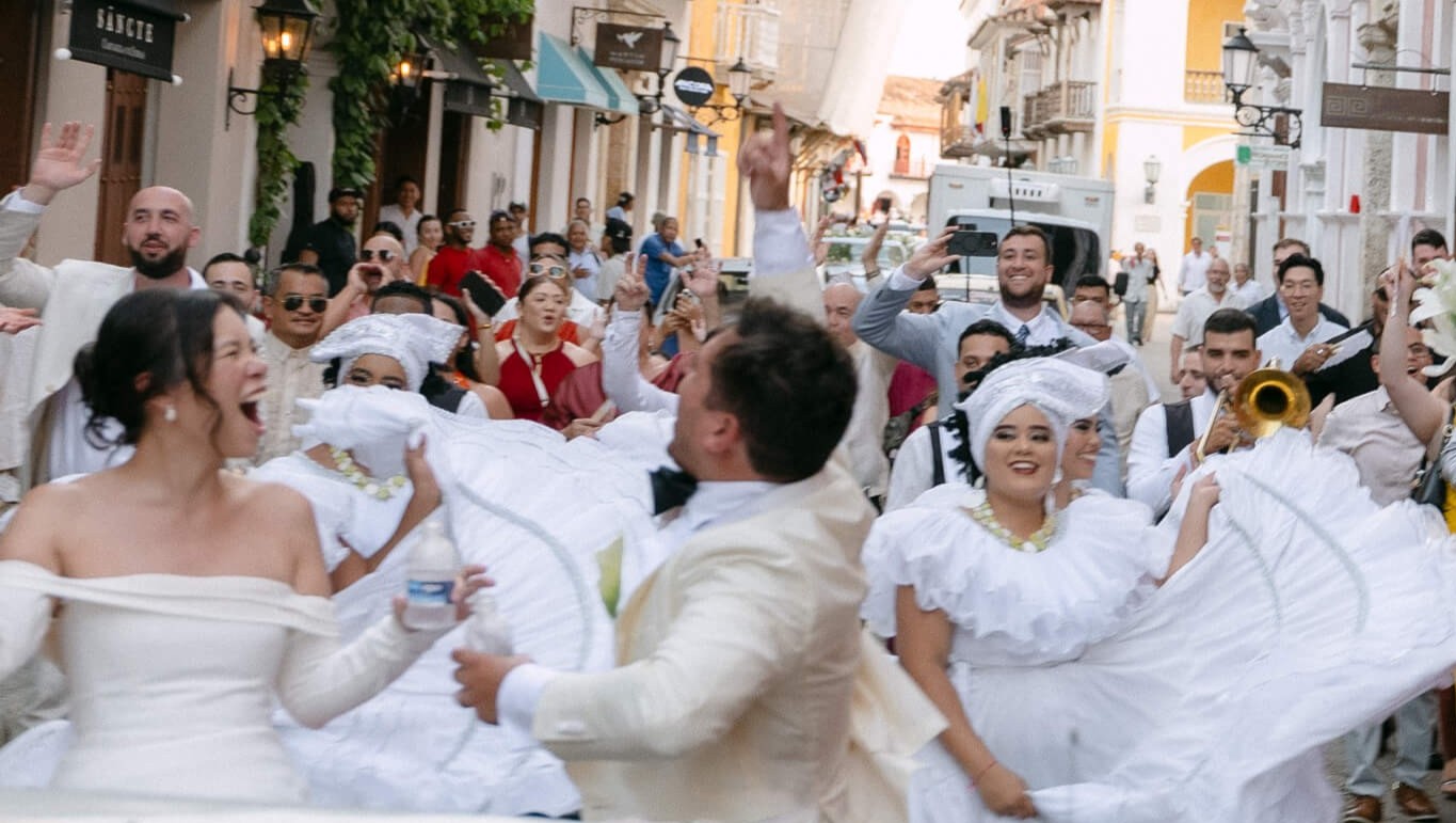 cartagena wedding photo in black and white couple riding in vintage car with their families behind them