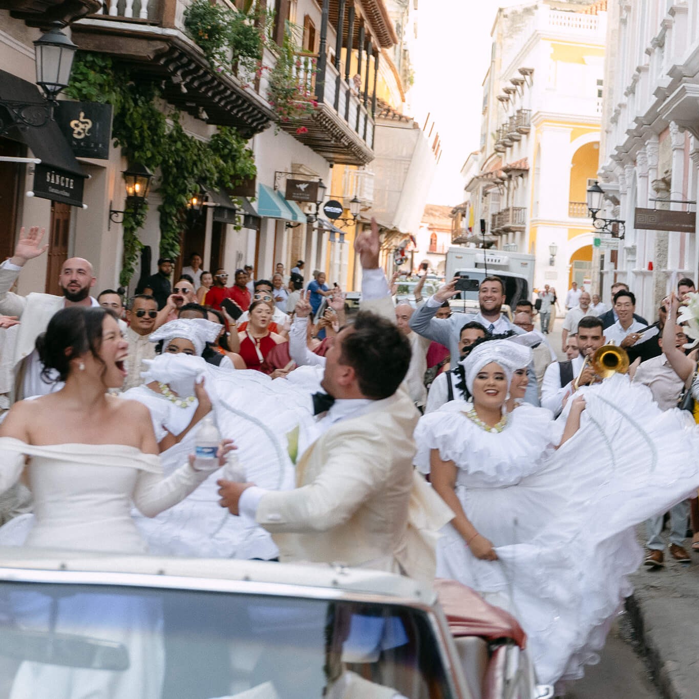 cartagena wedding photo in black and white couple riding in vintage car with their families behind them