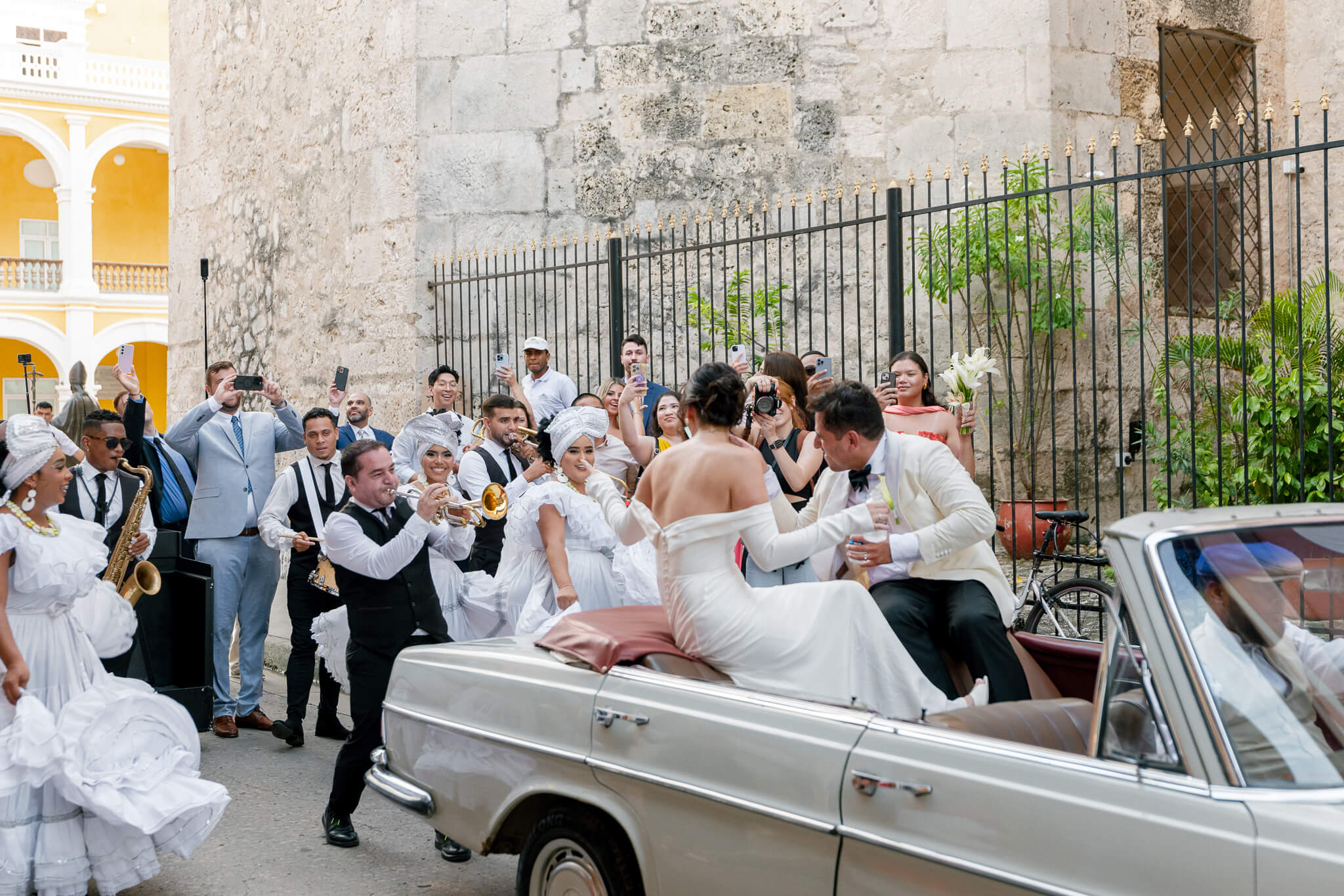 cartagena wedding couple dancing with band in vintage car through the streets and being surrounded by family and friends